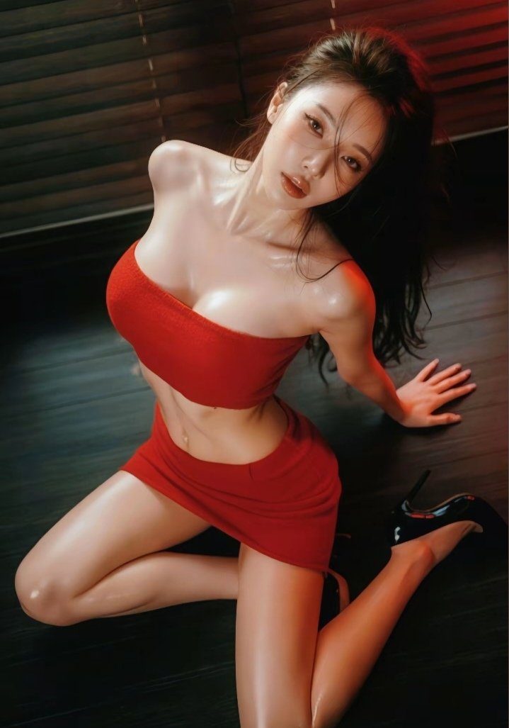 A woman in a red tube top and skirt poses indoors, wearing high heels.