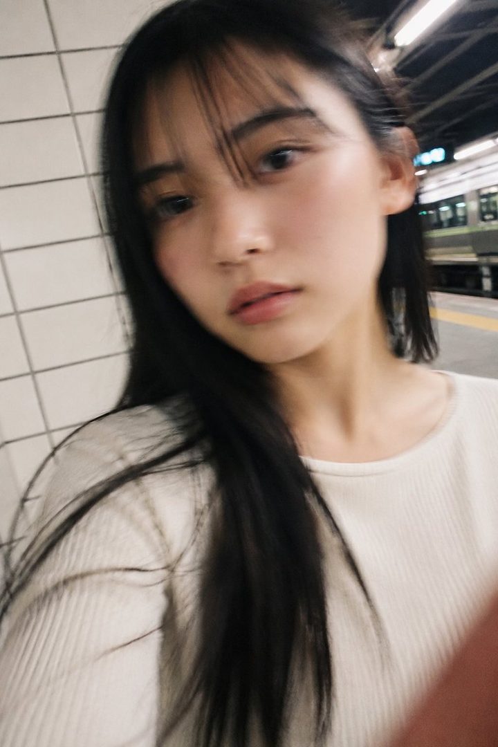 A young woman with long black hair and bangs takes a selfie in a train station at night.