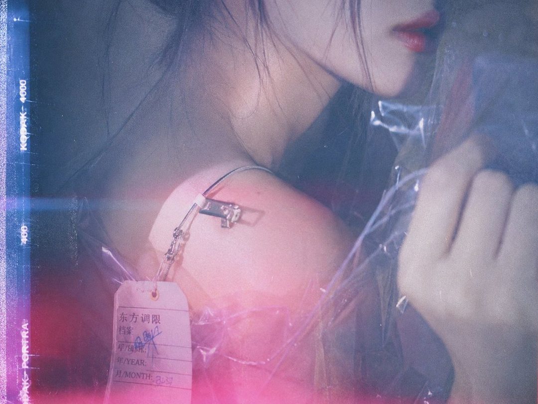 A close-up portrait of a woman's shoulder and neck, with a tag attached to her clothing, in a dreamy, futuristic style.