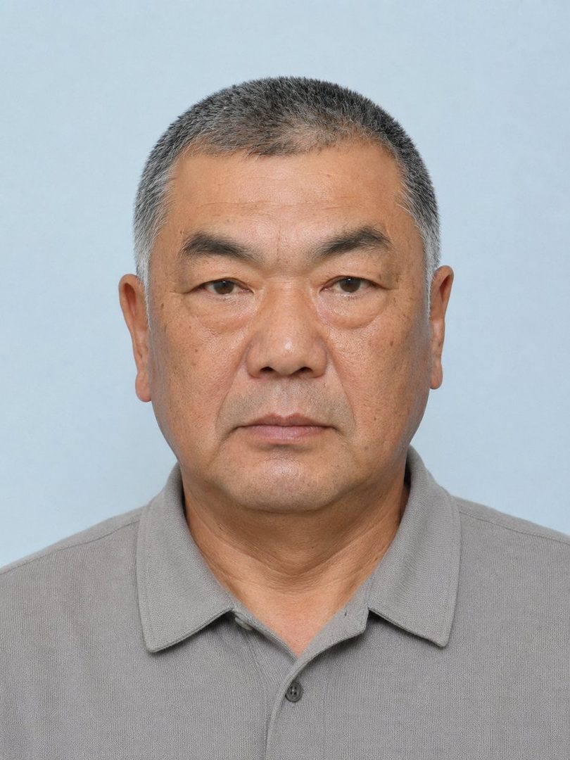 A studio portrait of an East Asian man with short gray hair and a gray polo shirt.