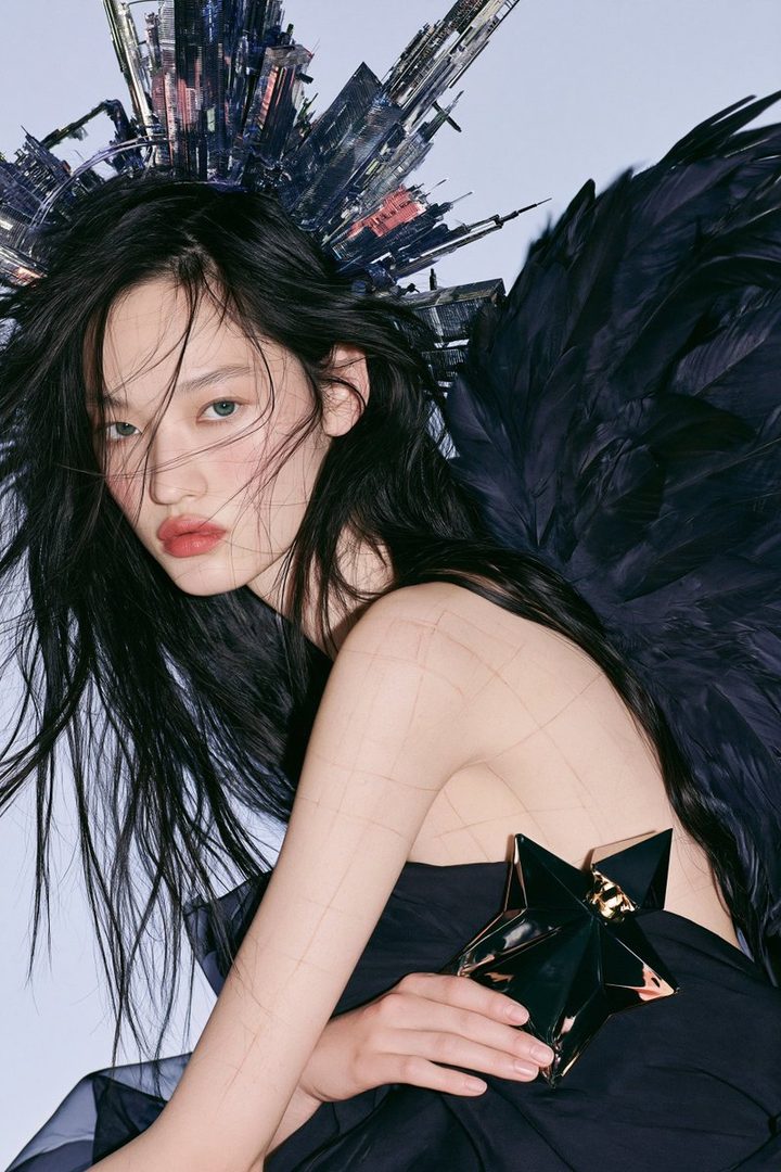 A striking portrait of an East Asian model with long black hair, wearing a black dress and adorned with large black wings and a futuristic headpiece, holding a star-shaped object.