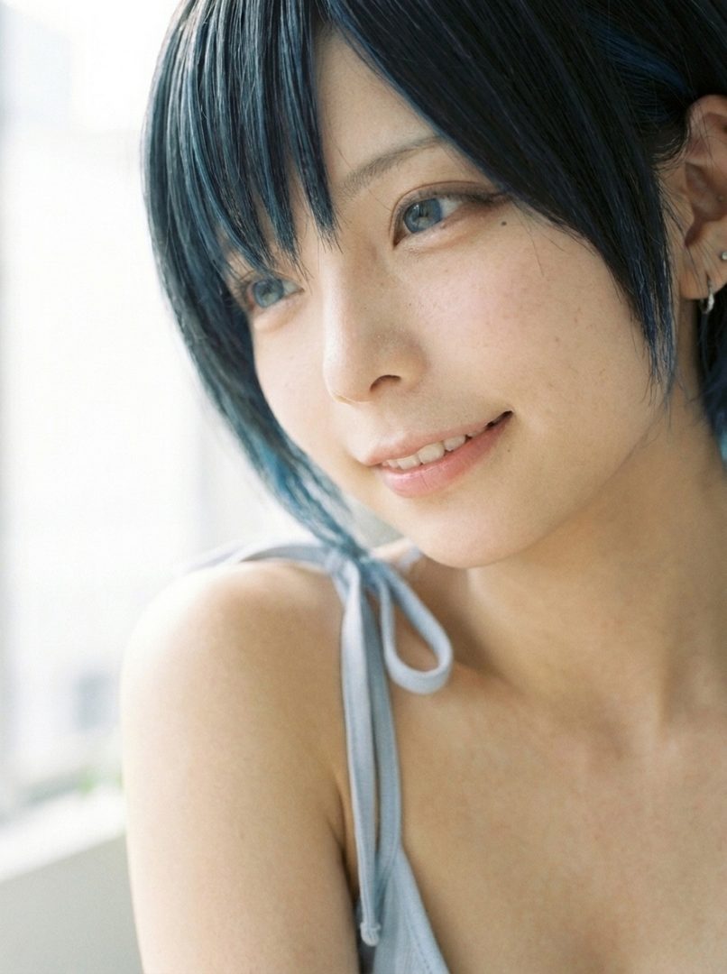 Close-up portrait of a young East Asian woman with short black hair and blue streaks, looking to the side with a gentle smile.