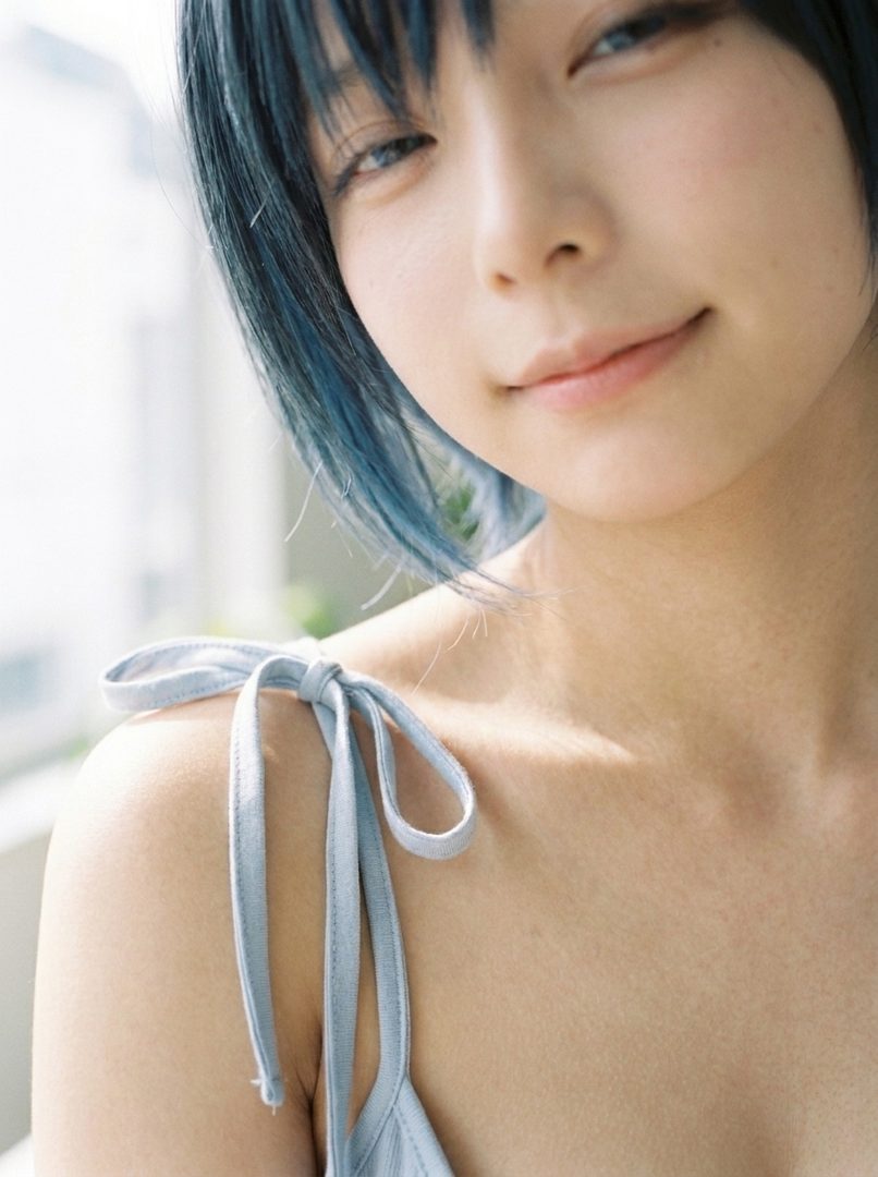 Close-up portrait of a young East Asian woman with short blue hair, smiling gently.
