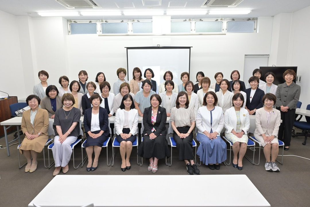 A group of Japanese women in business attire posing for a photo in an indoor meeting room.