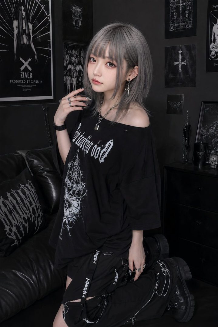A young woman with short, silver hair and bangs, wearing an off-the-shoulder black t-shirt with a graphic print and black pants, posing indoors with a dark, gothic-themed background.