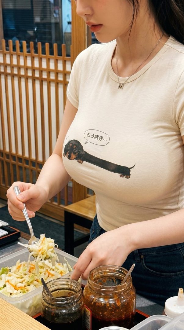 A woman in a casual t-shirt with a dachshund graphic is serving herself a salad at a restaurant.