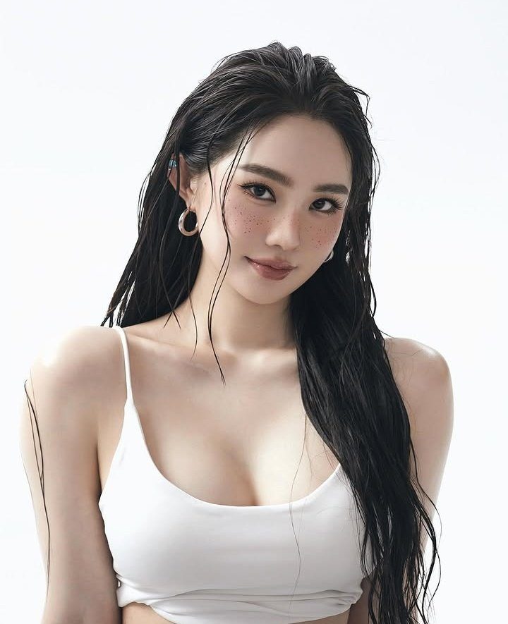 A beautiful East Asian woman with long black hair and freckles, wearing a white tank top, posing for a portrait.
