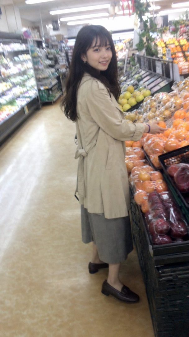 A young woman with long dark hair smiles while shopping for fruit in a supermarket aisle.
