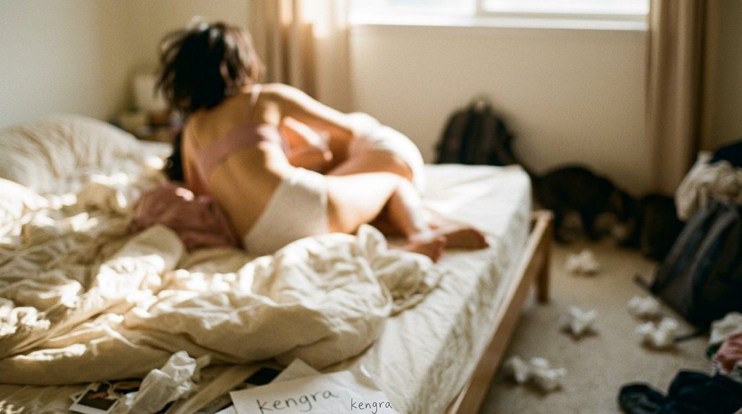 Two people embracing intimately on a messy bed in a sunlit room.