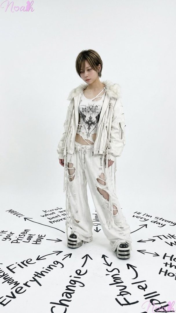 A person with short, highlighted hair wears a distressed white jacket, cropped graphic top, and ripped white pants with platform shoes, standing in a bright studio with text and arrows on the floor.
