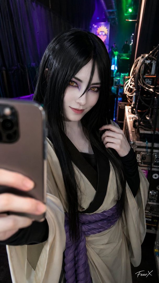A person in Orochimaru cosplay takes a selfie in a backstage area with stage equipment and lighting.