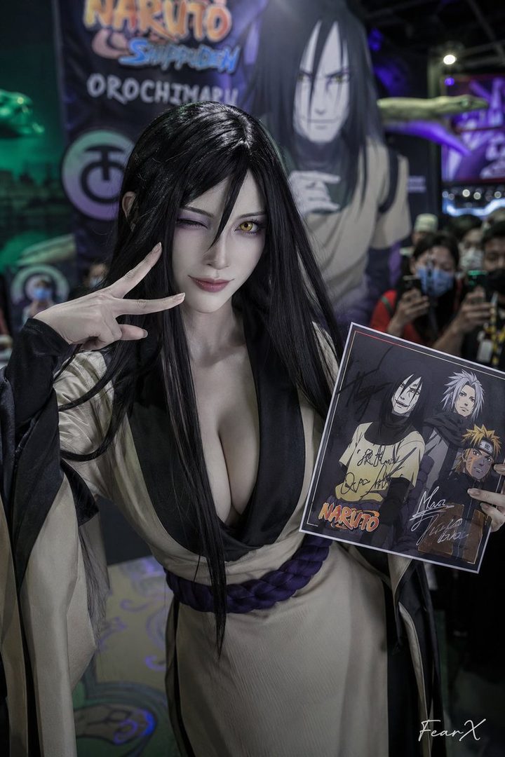 A cosplayer dressed as Orochimaru from Naruto poses with a peace sign and holds a signed Naruto poster.