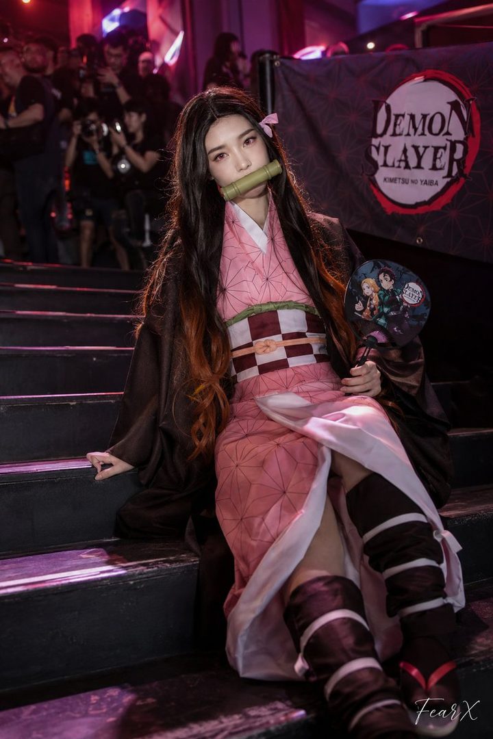 A cosplayer dressed as Nezuko Kamado from Demon Slayer sits on stairs, holding a fan.