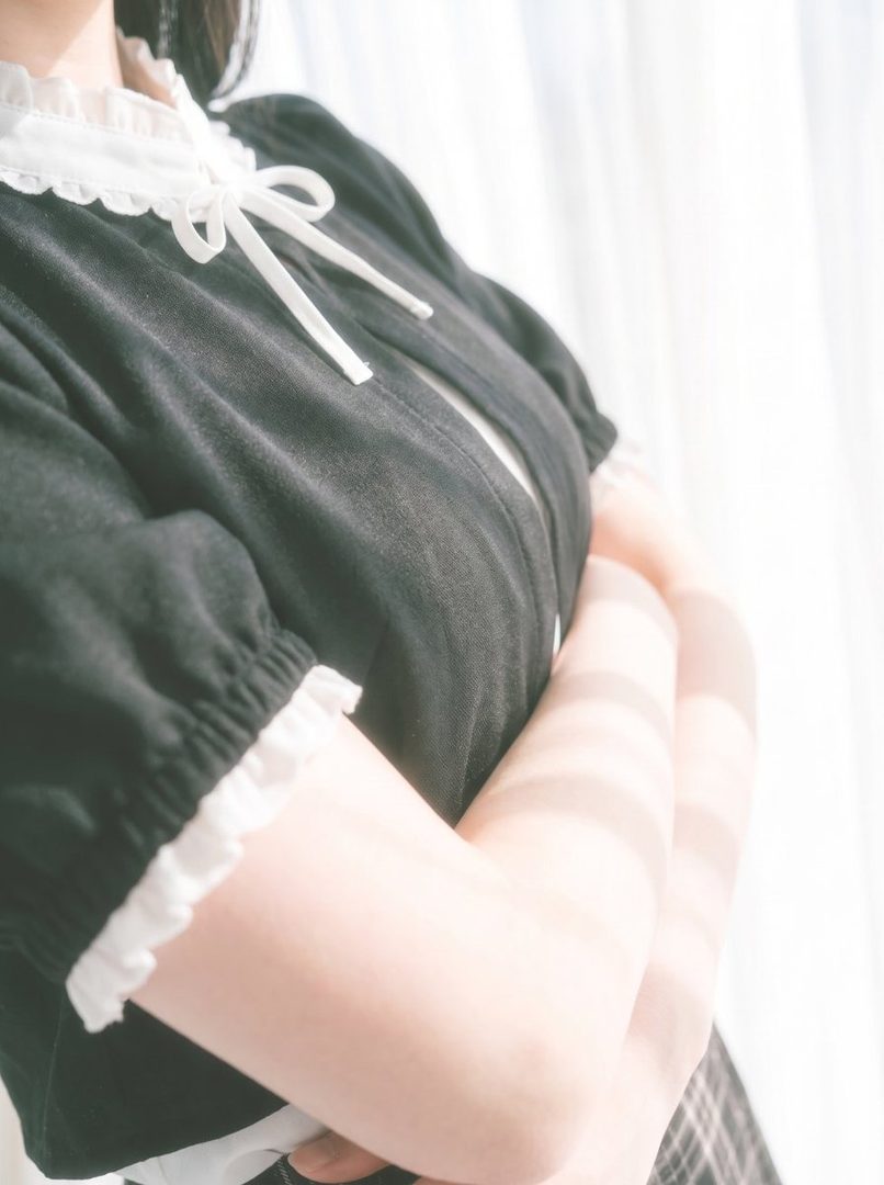 A close-up shot of a person wearing a black maid outfit with white frills and a bow, with their arms crossed.
