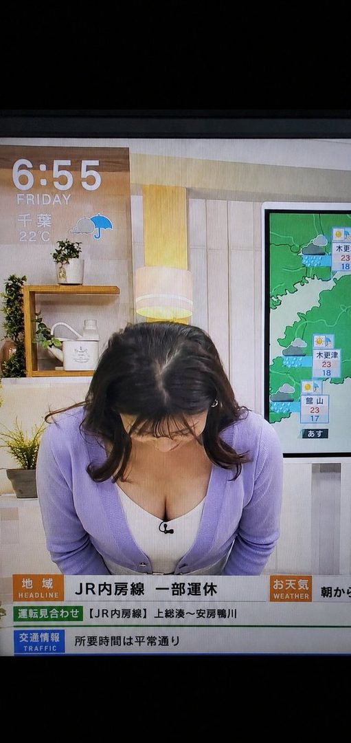 A woman with long dark hair, wearing a lavender cardigan and white top, bows in what appears to be a news studio setting, with a weather map and news headlines visible in the background.