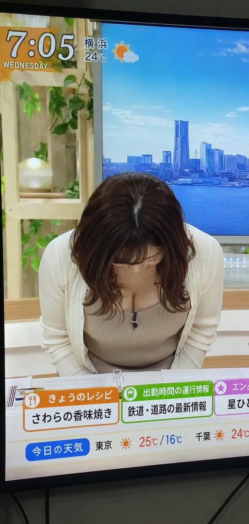 A woman with brown hair bows while wearing a beige top and white cardigan, displayed on a television screen showing news graphics.