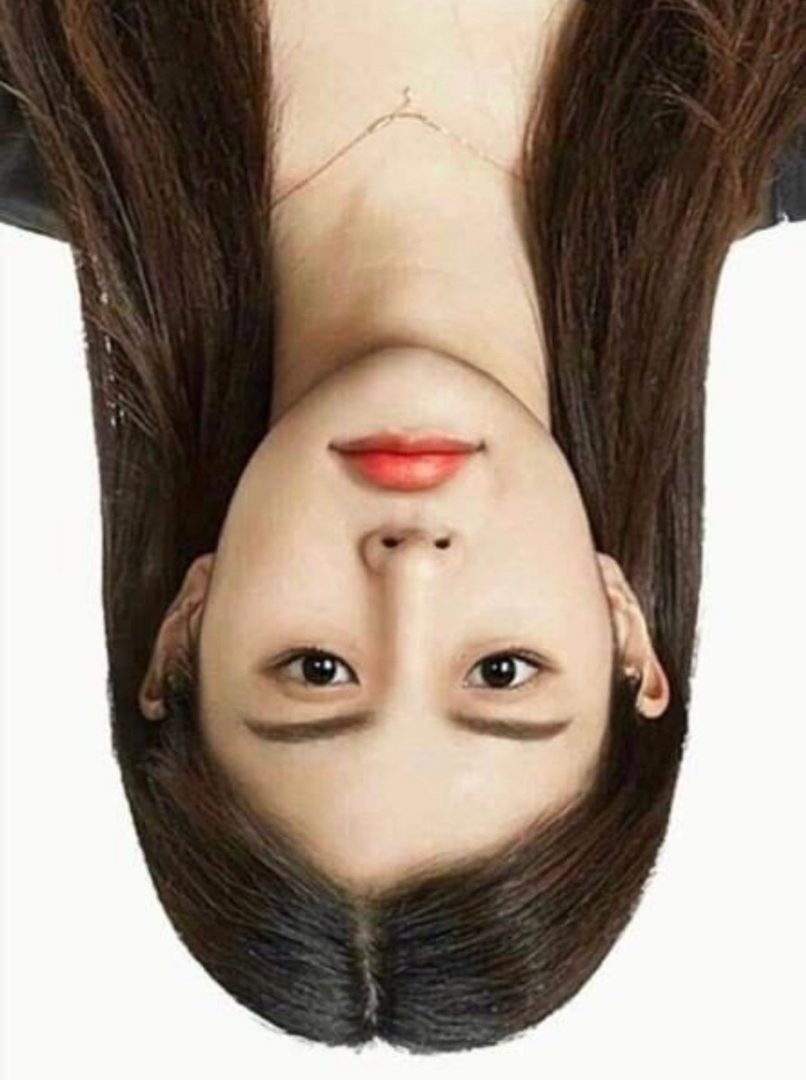 An upside-down portrait of a young East Asian woman with long brown hair, wearing subtle makeup and a delicate necklace.