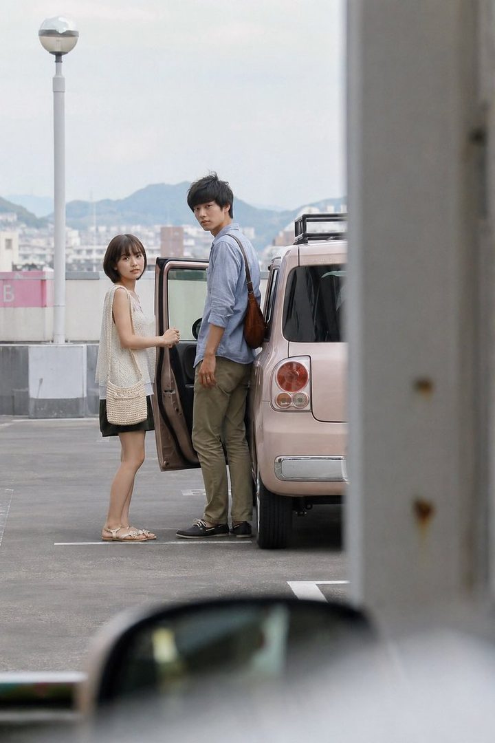 A young Japanese couple standing next to a car in a parking lot.