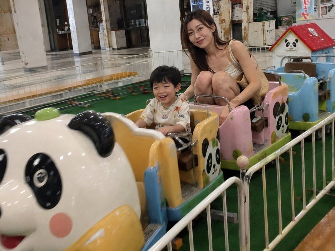 A young East Asian woman and a child are riding a panda-themed amusement park ride indoors.