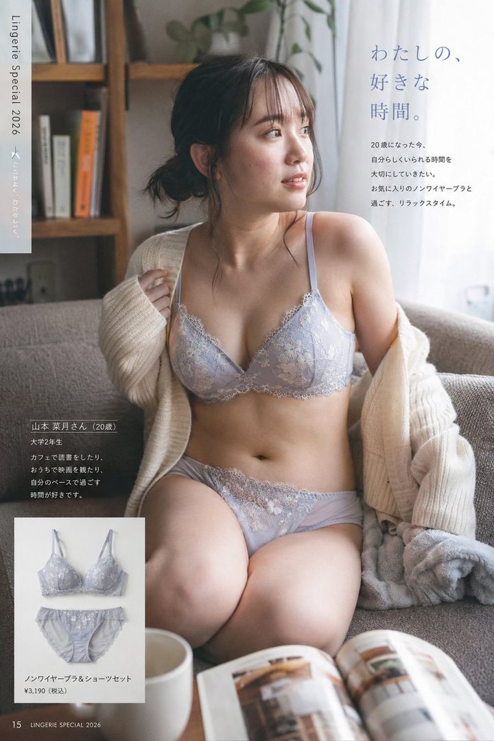 A young woman with dark hair in a messy bun wears a light purple lace lingerie set and a cream cardigan, sitting on a sofa in a cozy room with a book.