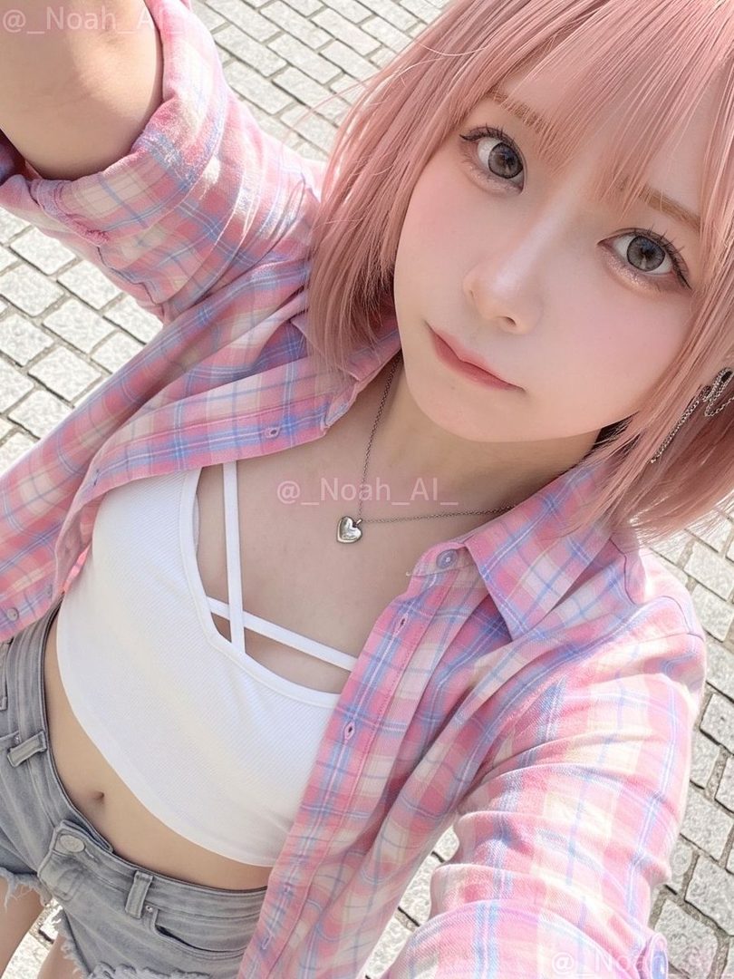 A young woman with short pink hair and a pink plaid shirt over a white crop top and denim shorts takes a selfie outdoors.