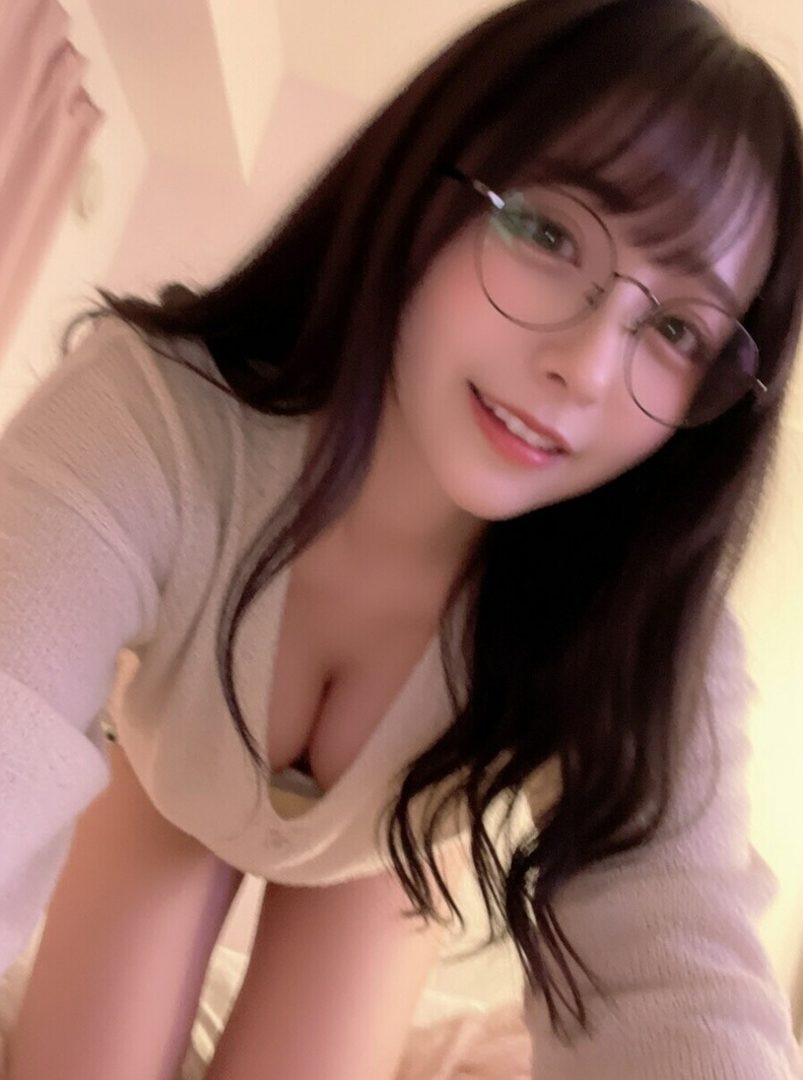 A young woman with long dark hair and glasses smiles at the camera, wearing a white sweater.