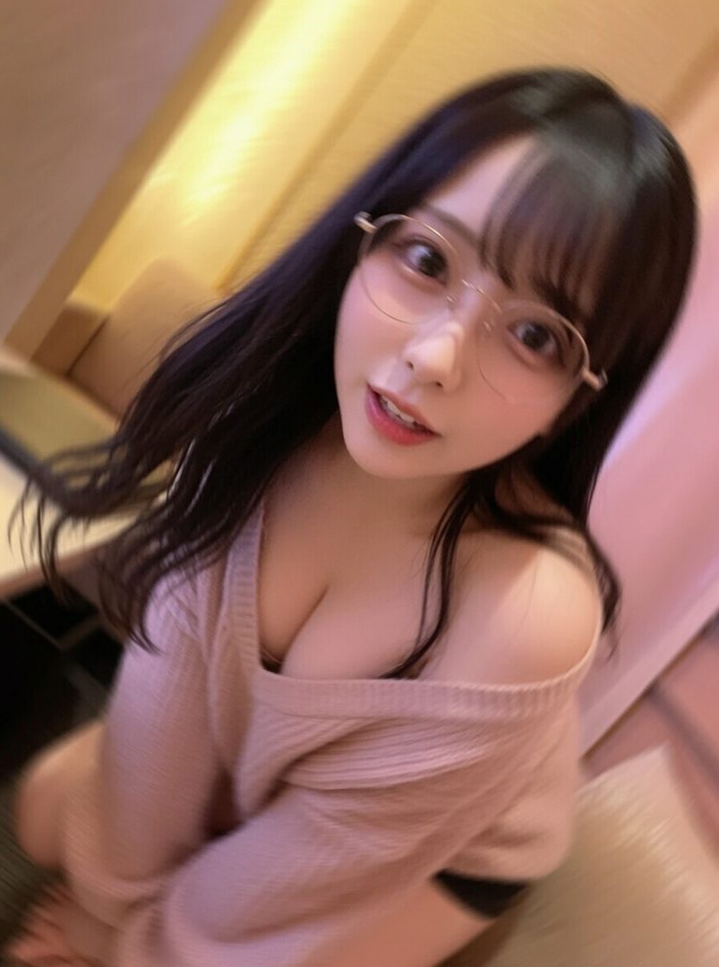 A young East Asian woman with long black hair and bangs, wearing glasses and an off-the-shoulder sweater, poses for a selfie indoors.