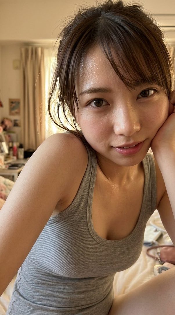 A close-up selfie of a young East Asian woman with brown hair, wearing a grey tank top, with a slightly sweaty complexion, looking at the camera with a gentle smile.