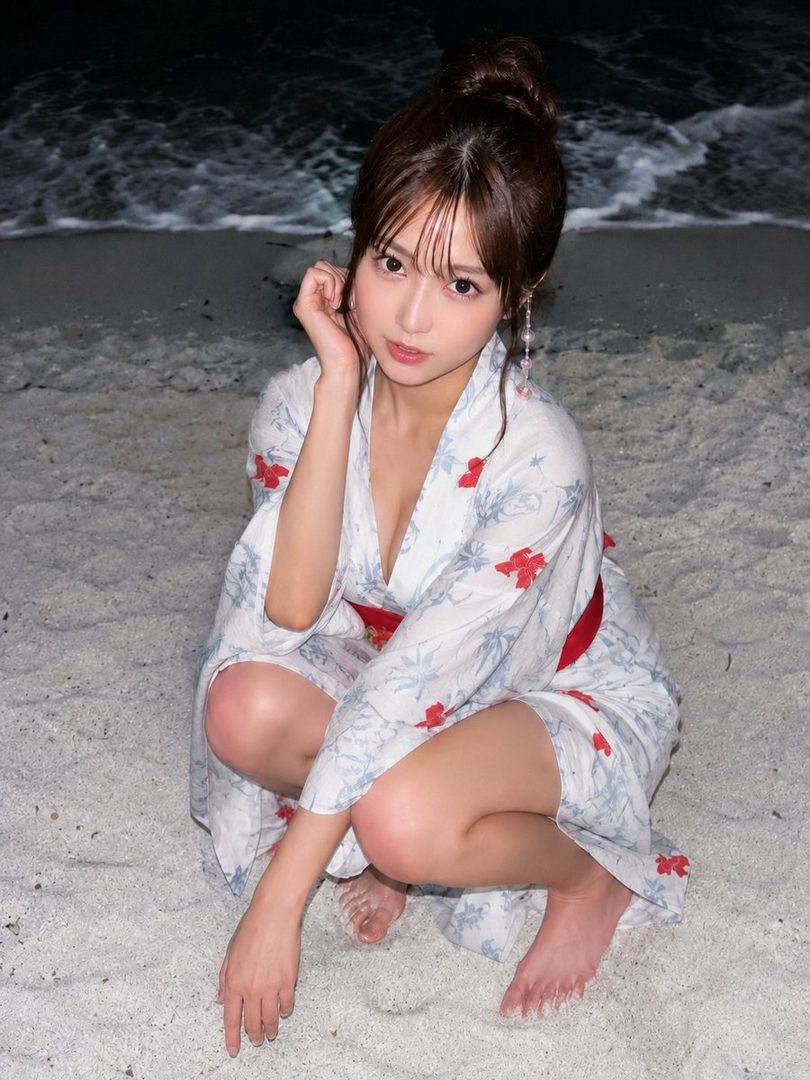A Japanese woman in a yukata crouches on a sandy beach at night, with the ocean waves in the background.