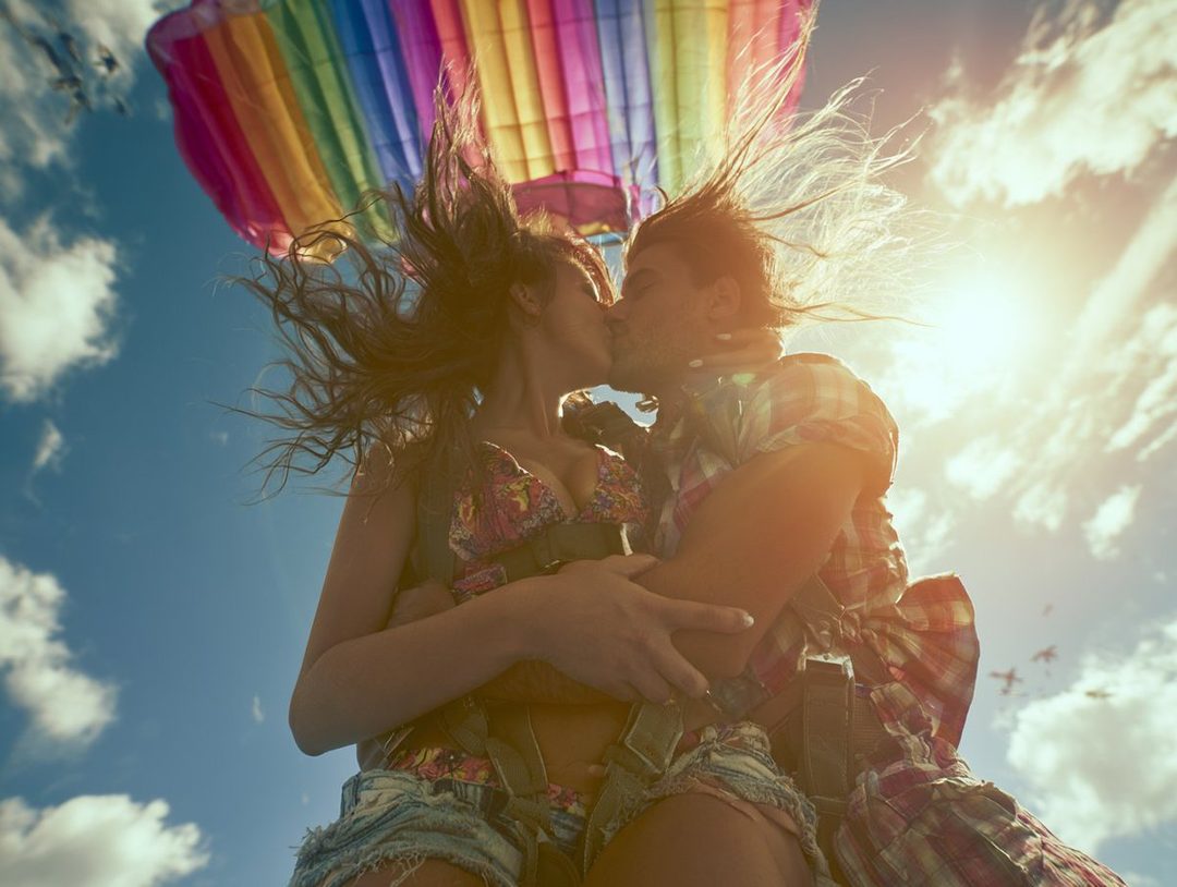 A couple kissing while skydiving with a rainbow parachute.