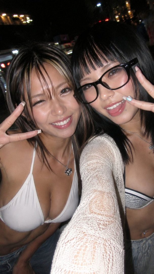 Two young women in bikinis taking a selfie at night, one wearing glasses and making a peace sign.