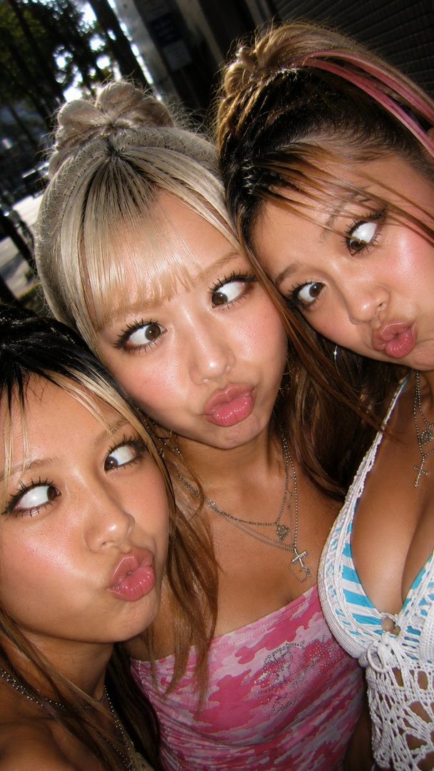Three young East Asian women with playful expressions and pouty lips, posing for a selfie outdoors.