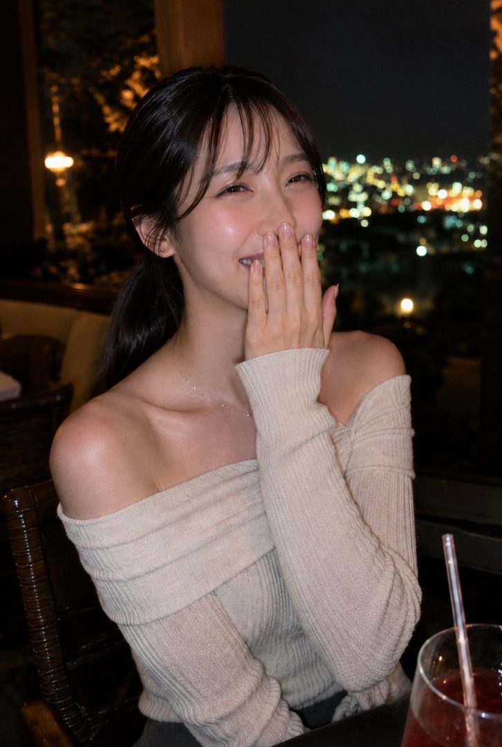 A young East Asian woman with dark hair, wearing an off-the-shoulder sweater, laughs with her hand covering her mouth, with a city skyline visible in the background at night.