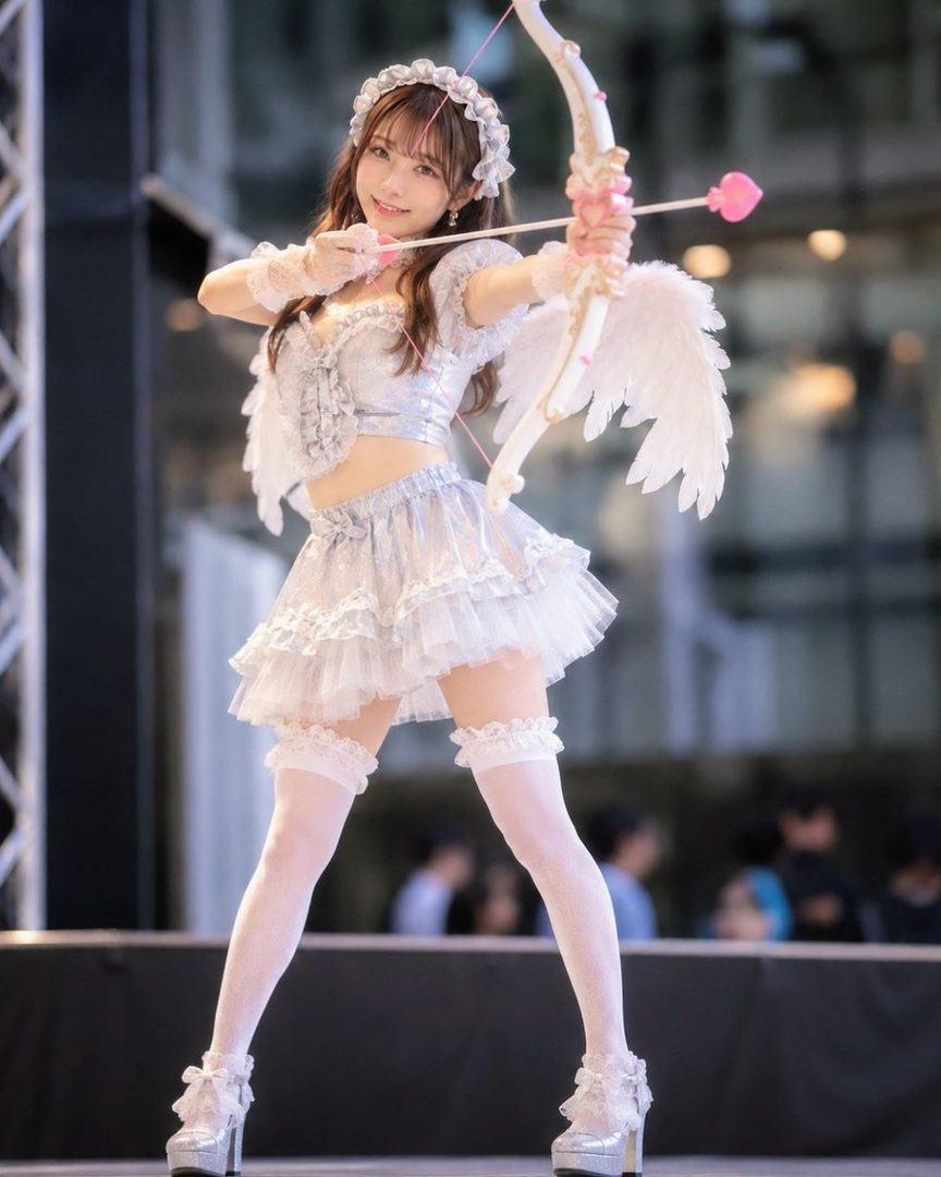 A young woman in an angel costume with wings and a bow and arrow, posing playfully.