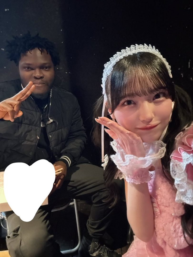 A young woman in a pink maid outfit with pigtails poses for a photo with a man.