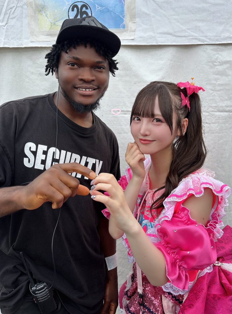 A security guard poses with a young woman in a bright pink idol outfit.