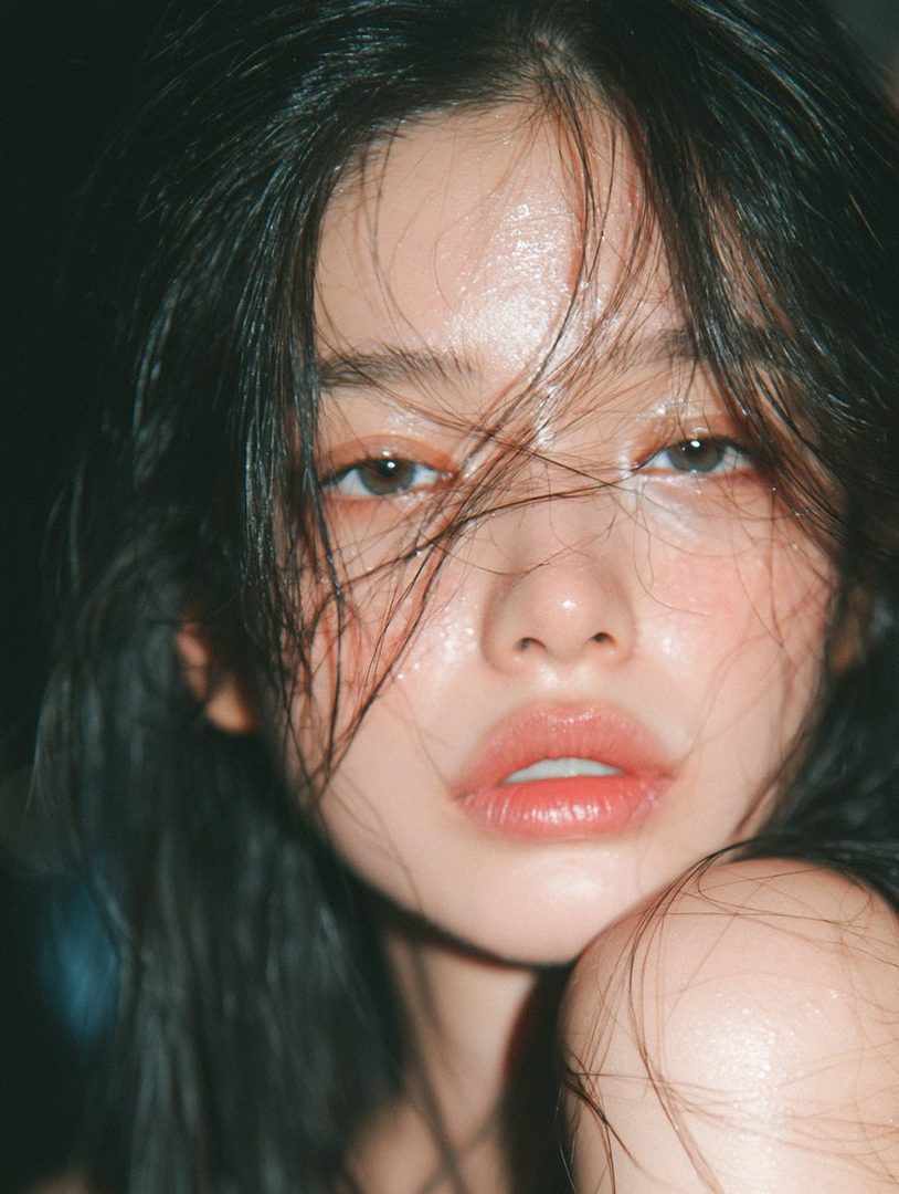 Close-up portrait of a young East Asian woman with wet, dark hair and dewy skin, looking directly at the camera with a soft expression.