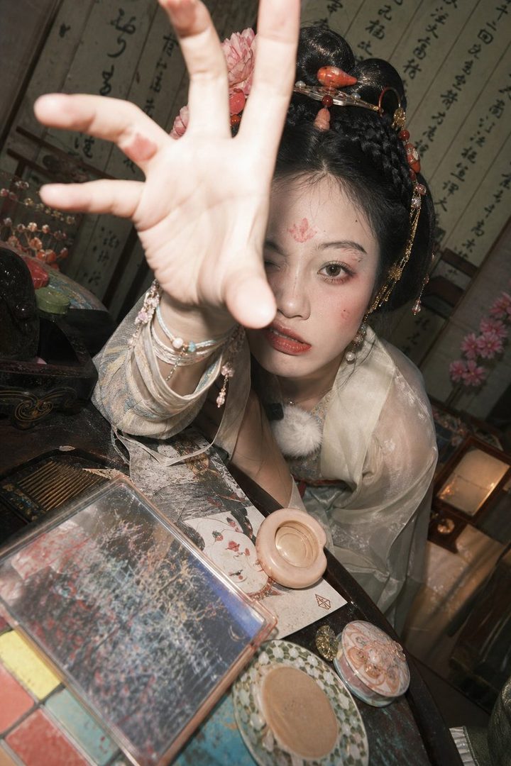 A young woman with traditional East Asian makeup and hairstyle reaches out towards the camera.