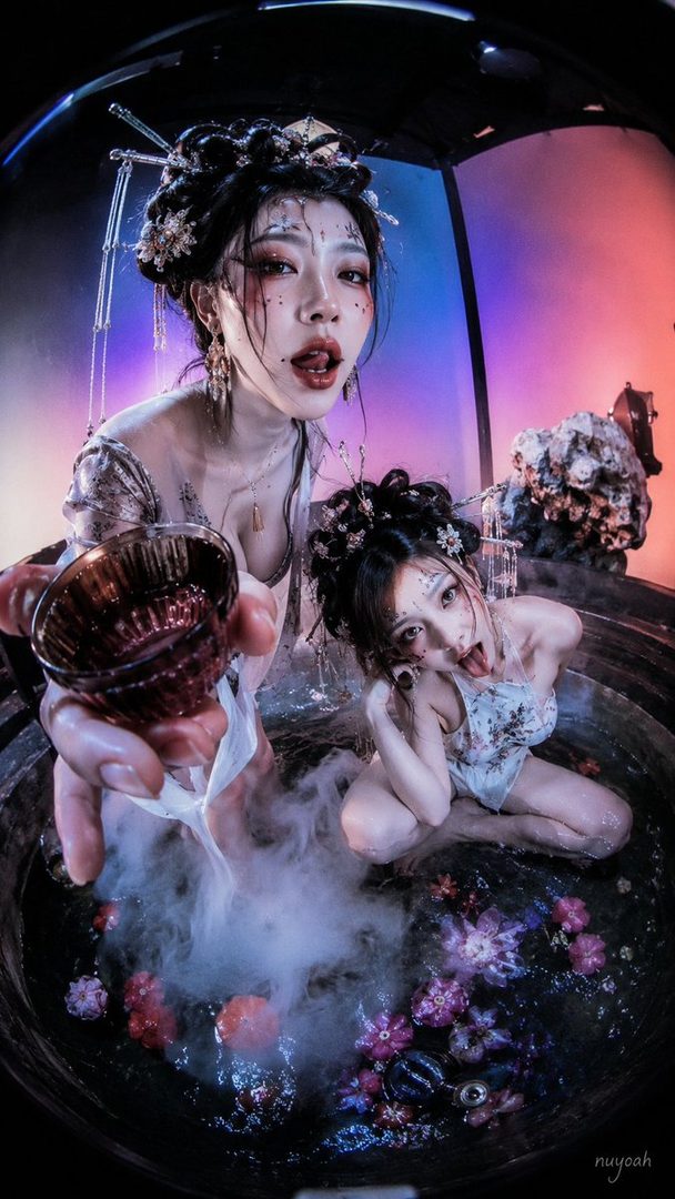 Two AI-generated women in traditional East Asian-inspired outfits with elaborate hairstyles and makeup, posing in a steamy, flower-filled bath with dramatic lighting.