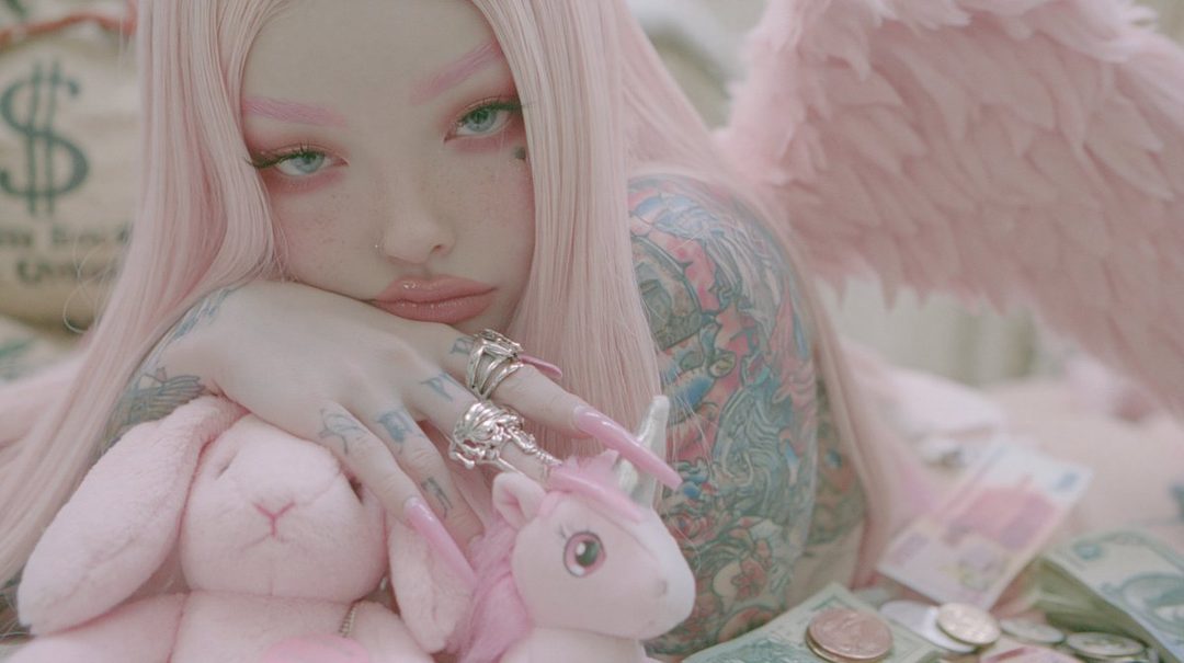 A young woman with long pink hair, pink eyebrows, and tattoos, posing with stuffed animals and money.