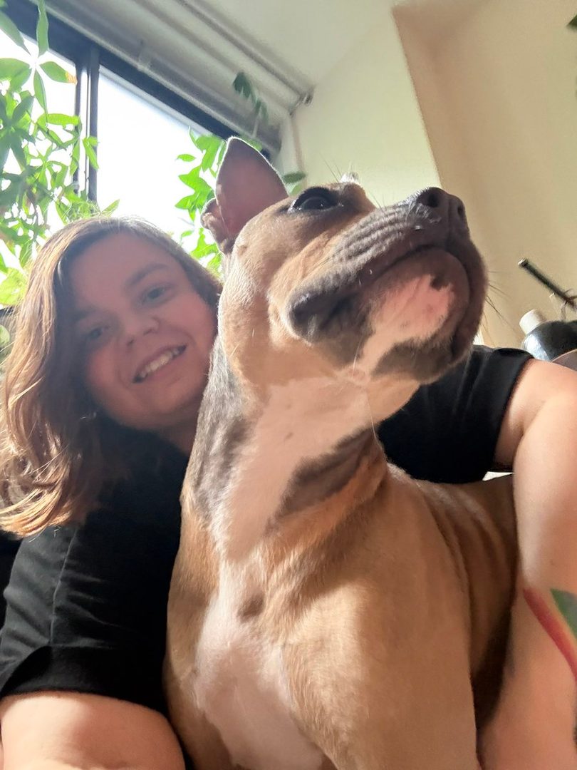 A person smiles while holding a dog in a selfie.