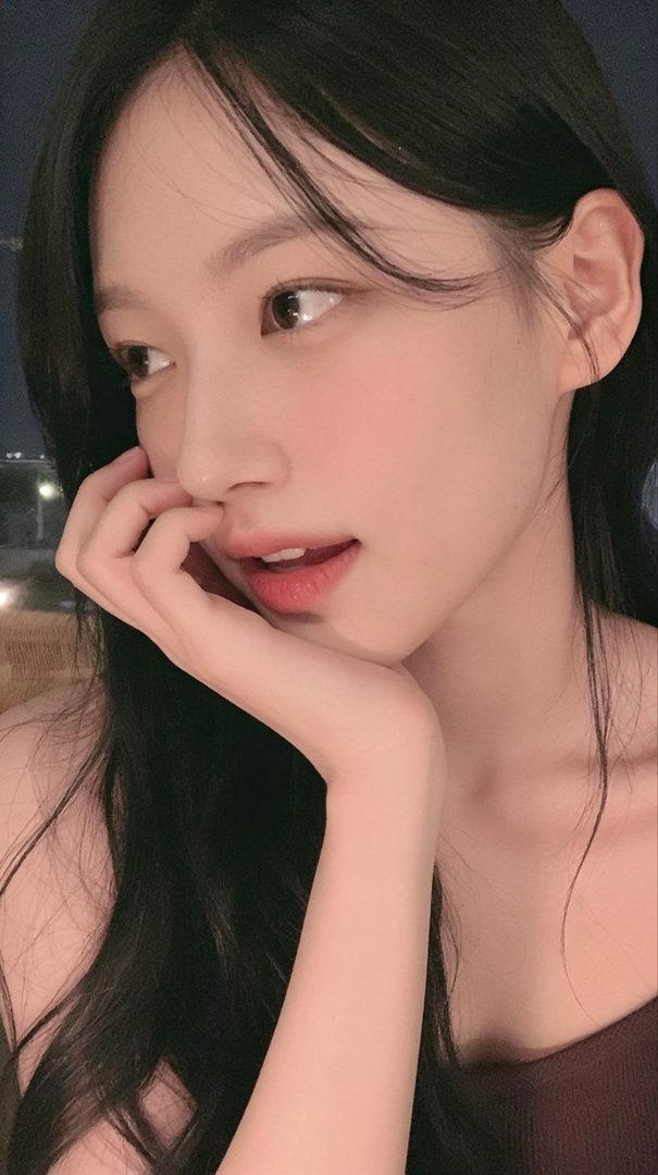 Close-up portrait of a young East Asian woman with long black hair, looking to the side with a gentle expression.
