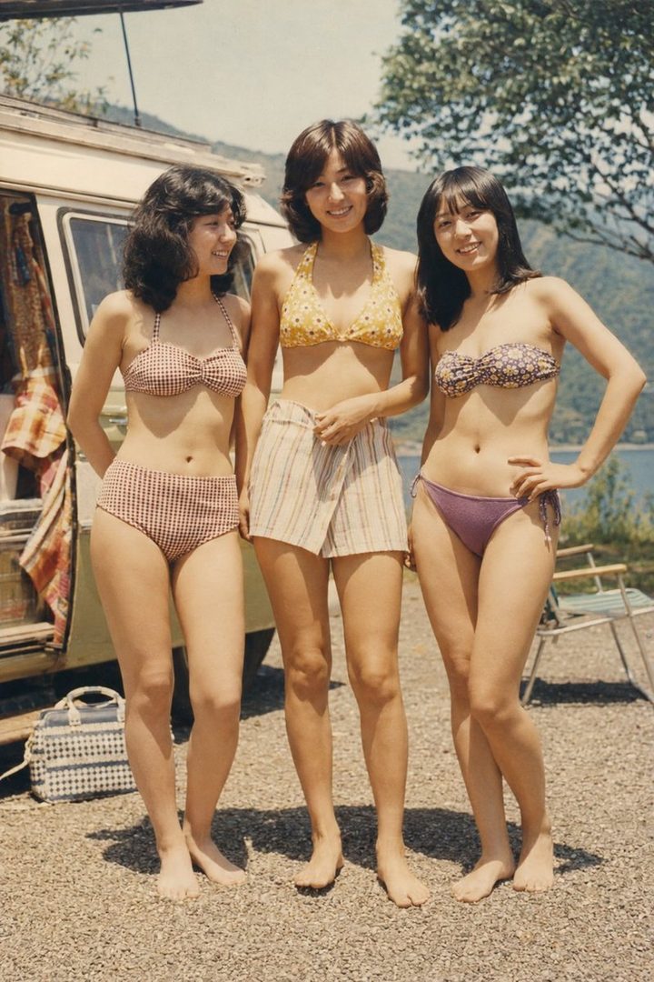 Three young women in retro bikinis and shorts stand barefoot by a lake with a camper van in the background, evoking a 1970s summer vibe.
