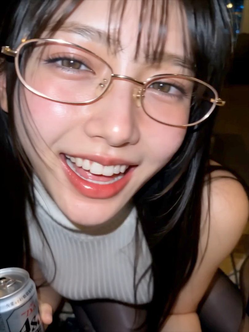 A close-up portrait of a smiling woman with black hair and glasses, wearing a white turtleneck and holding a beer can.