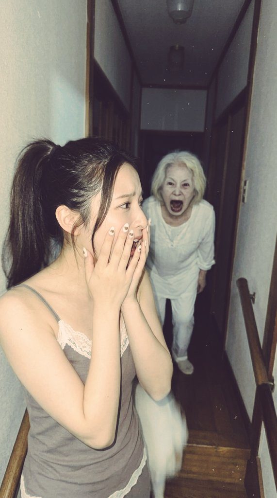 A young woman with a ponytail looks scared, covering her mouth with her hands, while an elderly woman with white hair and an open mouth appears behind her in a dimly lit hallway.