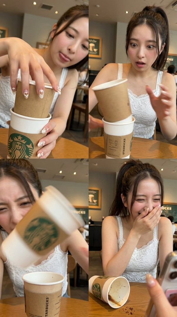 A young woman with long brown hair, wearing a white lace top, playfully interacts with Starbucks cups in a cafe, making funny faces and laughing.