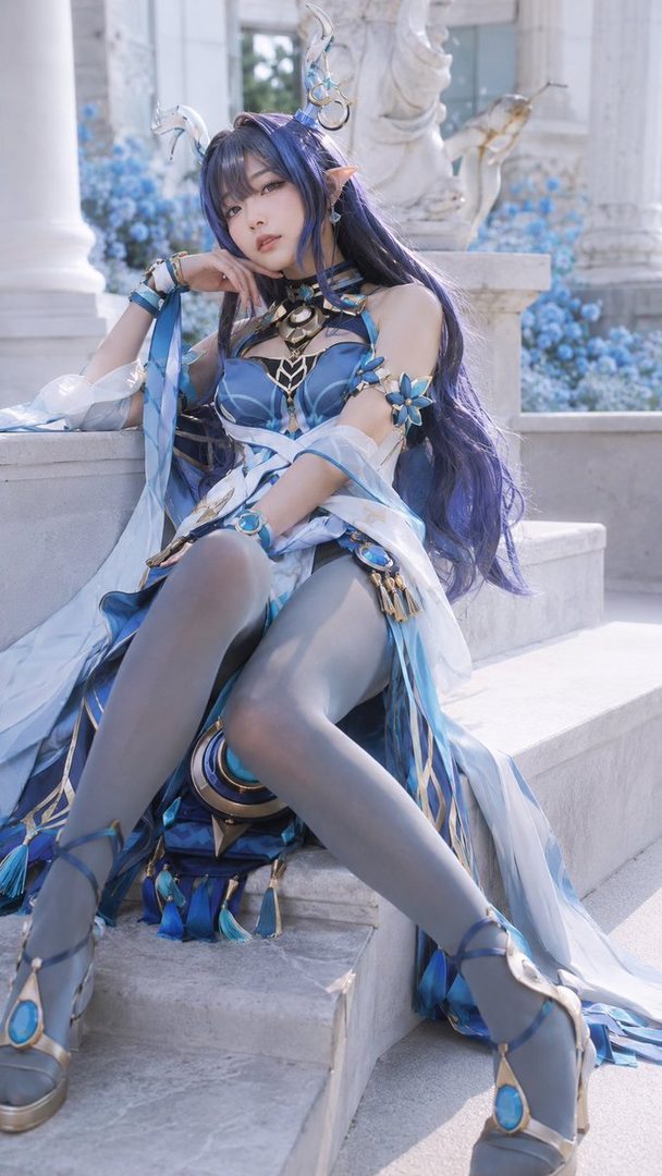 A woman in a blue fantasy-inspired costume with long purple hair, posing on outdoor stairs.