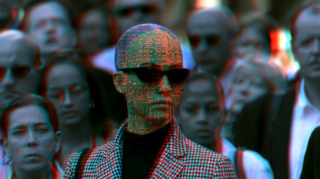 A person with a digitally textured face wearing sunglasses and a patterned jacket, surrounded by a blurred crowd.
