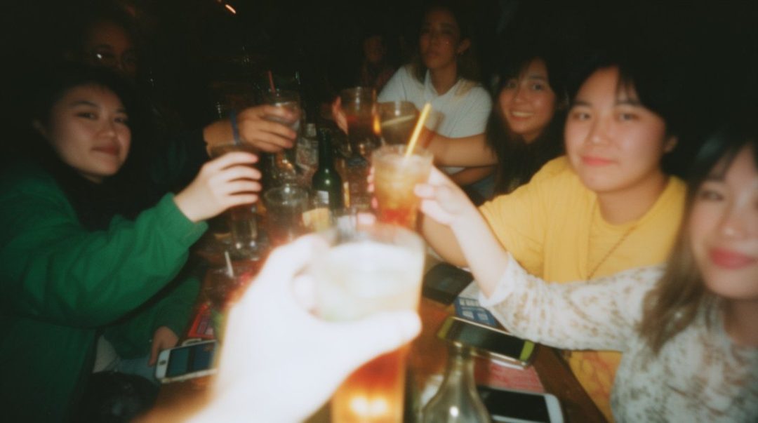 A group of young East Asian women toasting drinks at a dimly lit bar on a Saturday night.