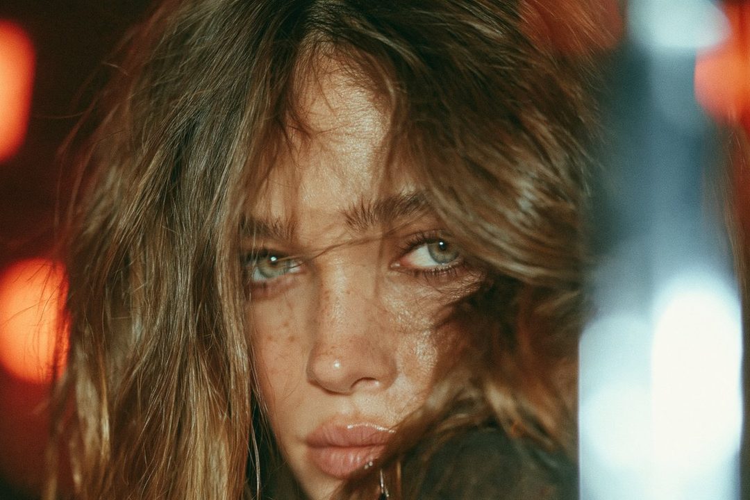 Close-up portrait of a young woman with light brown hair and green eyes, looking intensely at the camera.